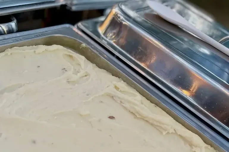 A full steam table pan of mashed potatoes beside two covered chafing dishes.