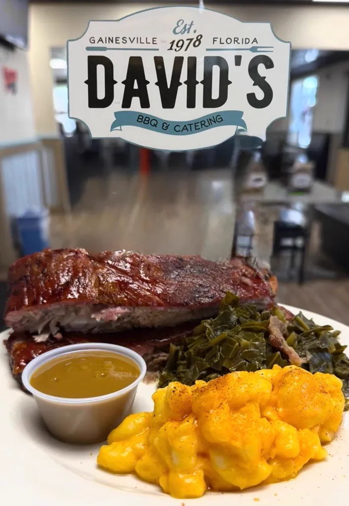 A rack of ribs with collards, mac and cheese, and a cup of mustard sauce, under the David's BBQ and Catering plaque