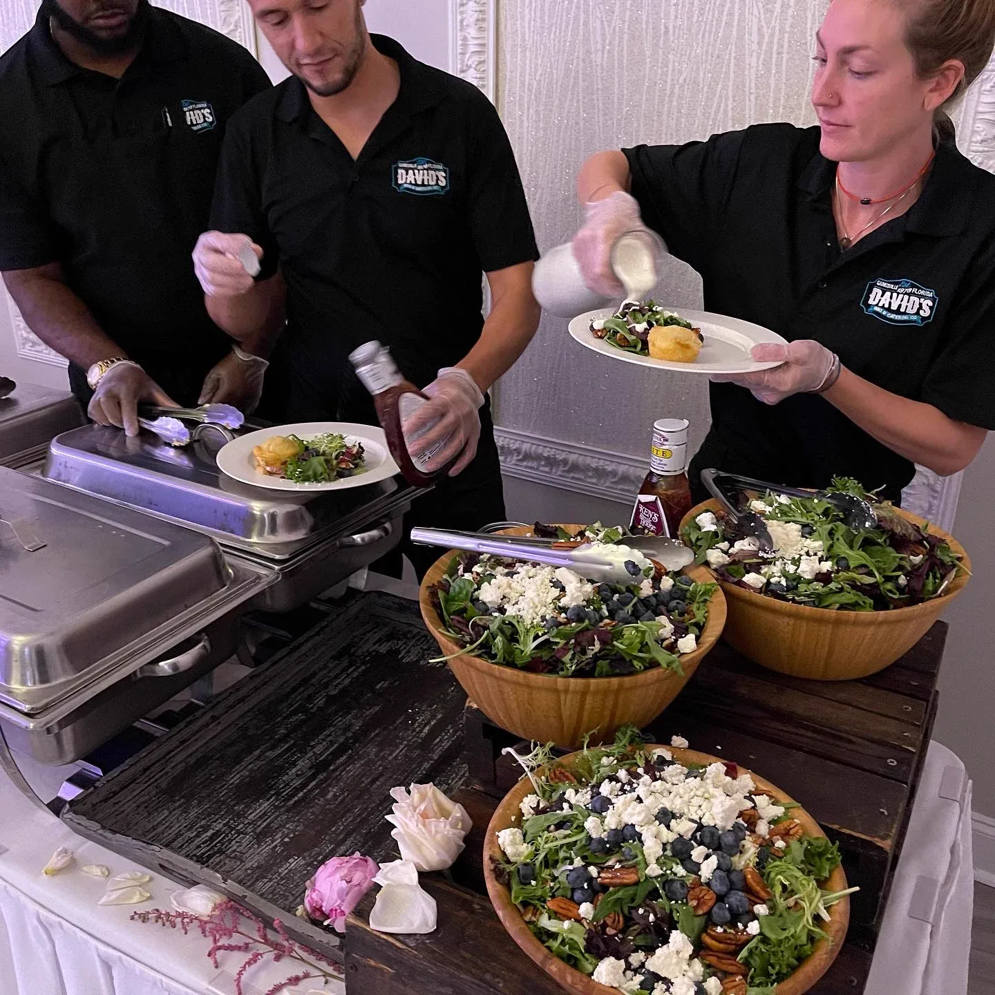 Three staff members plating salad from large wooden bowls