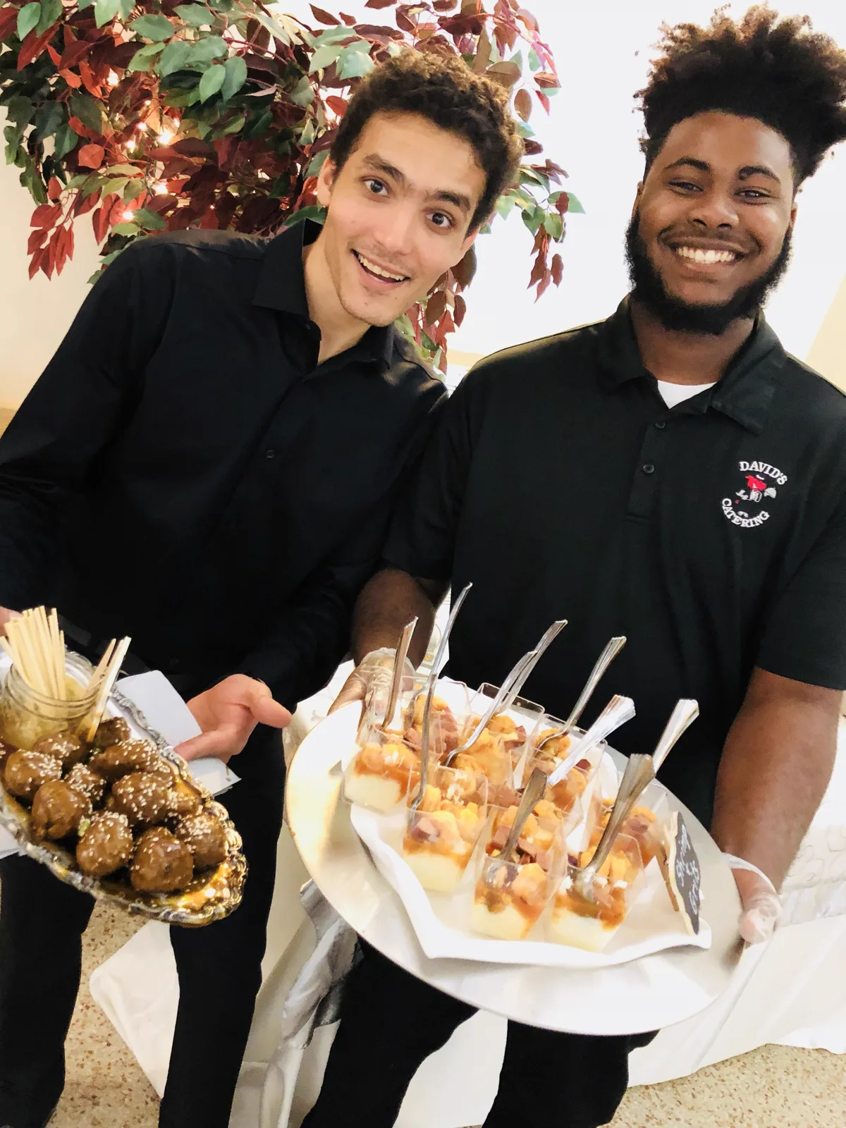 Two staff holding platters of glazed meatballs and shrimp and grits cups