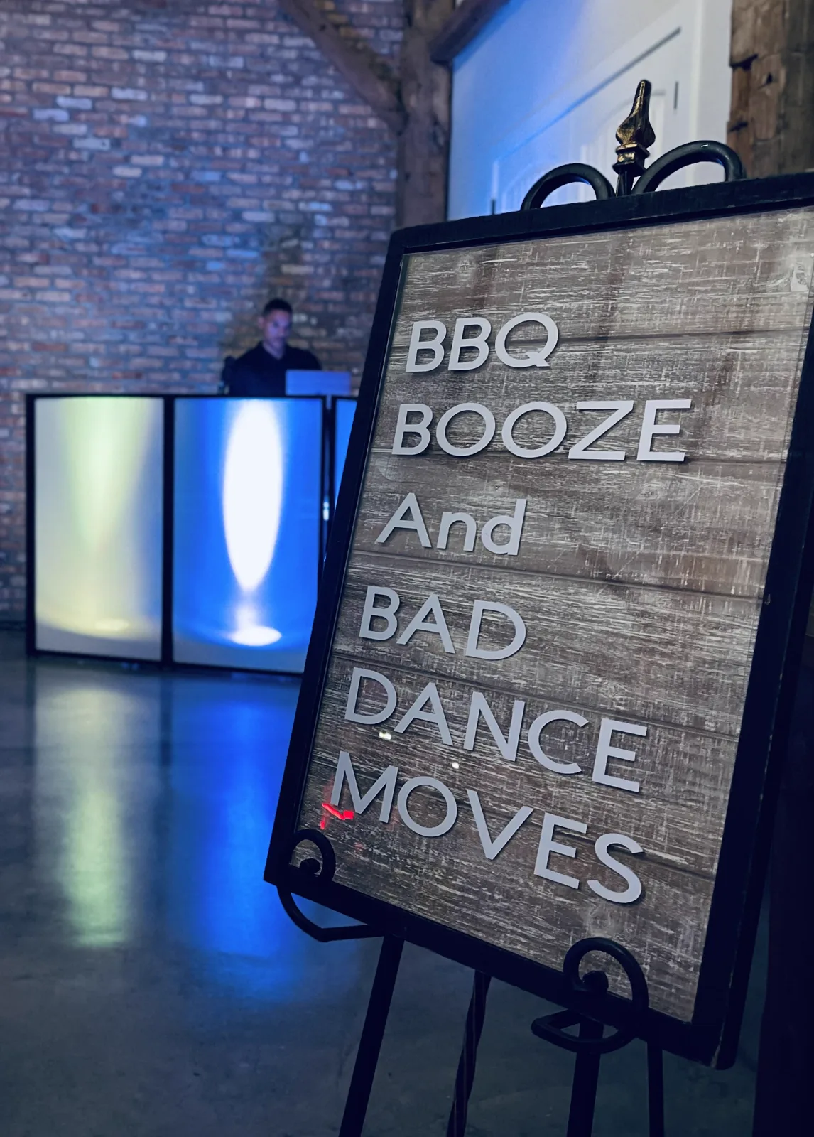 A wood plank sign on an easel reading BBQ, booze and bad dance moves