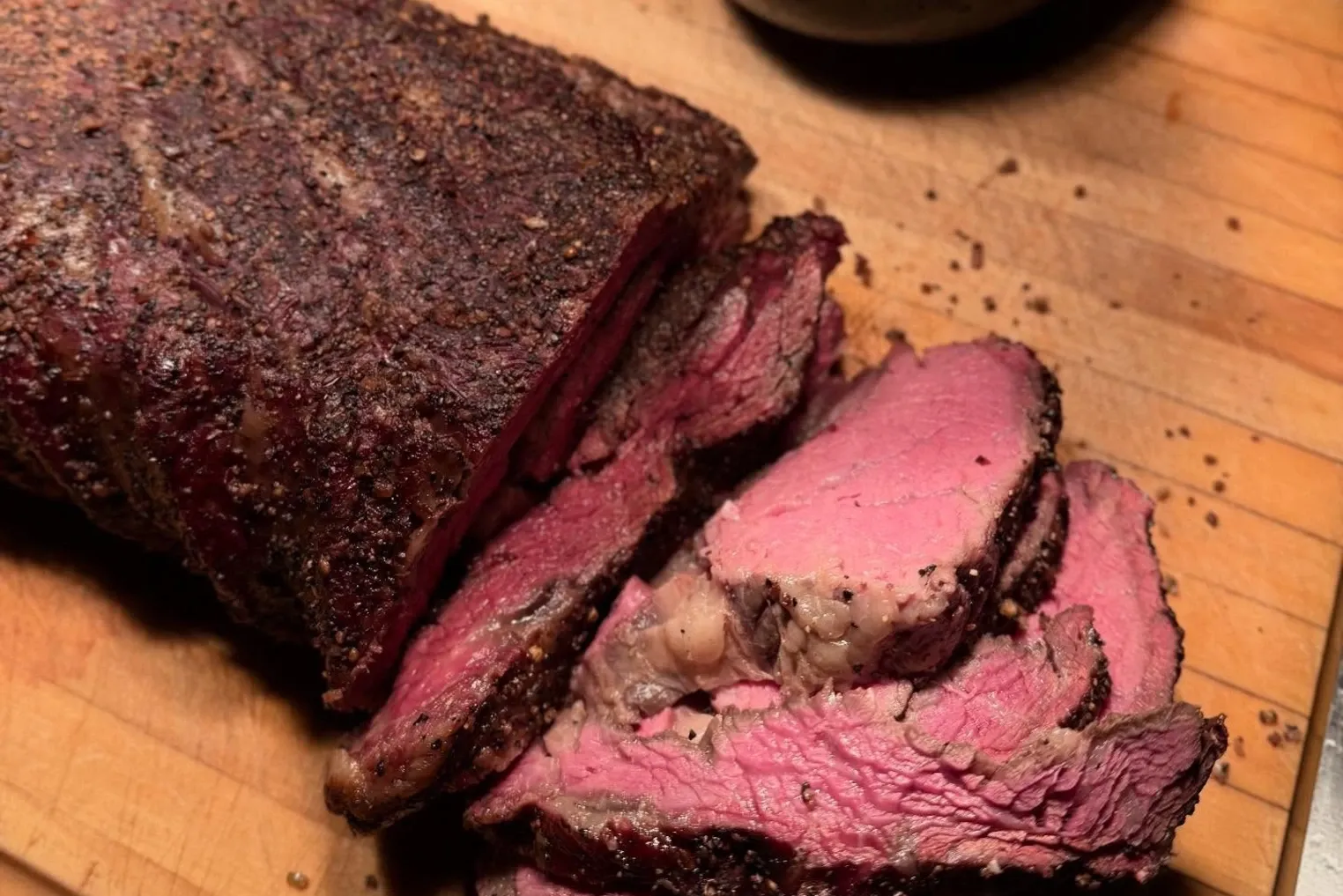 Sliced smoked beef with a rosy center on a carving board.