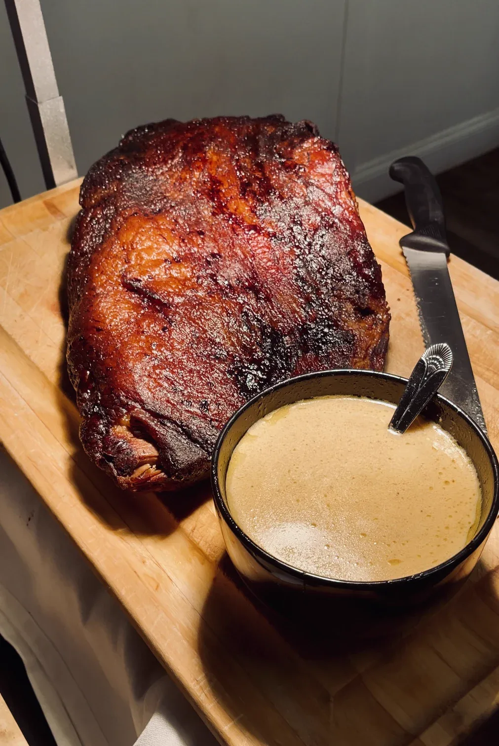 A glossy smoked roast on a board beside a bowl of creamy sauce