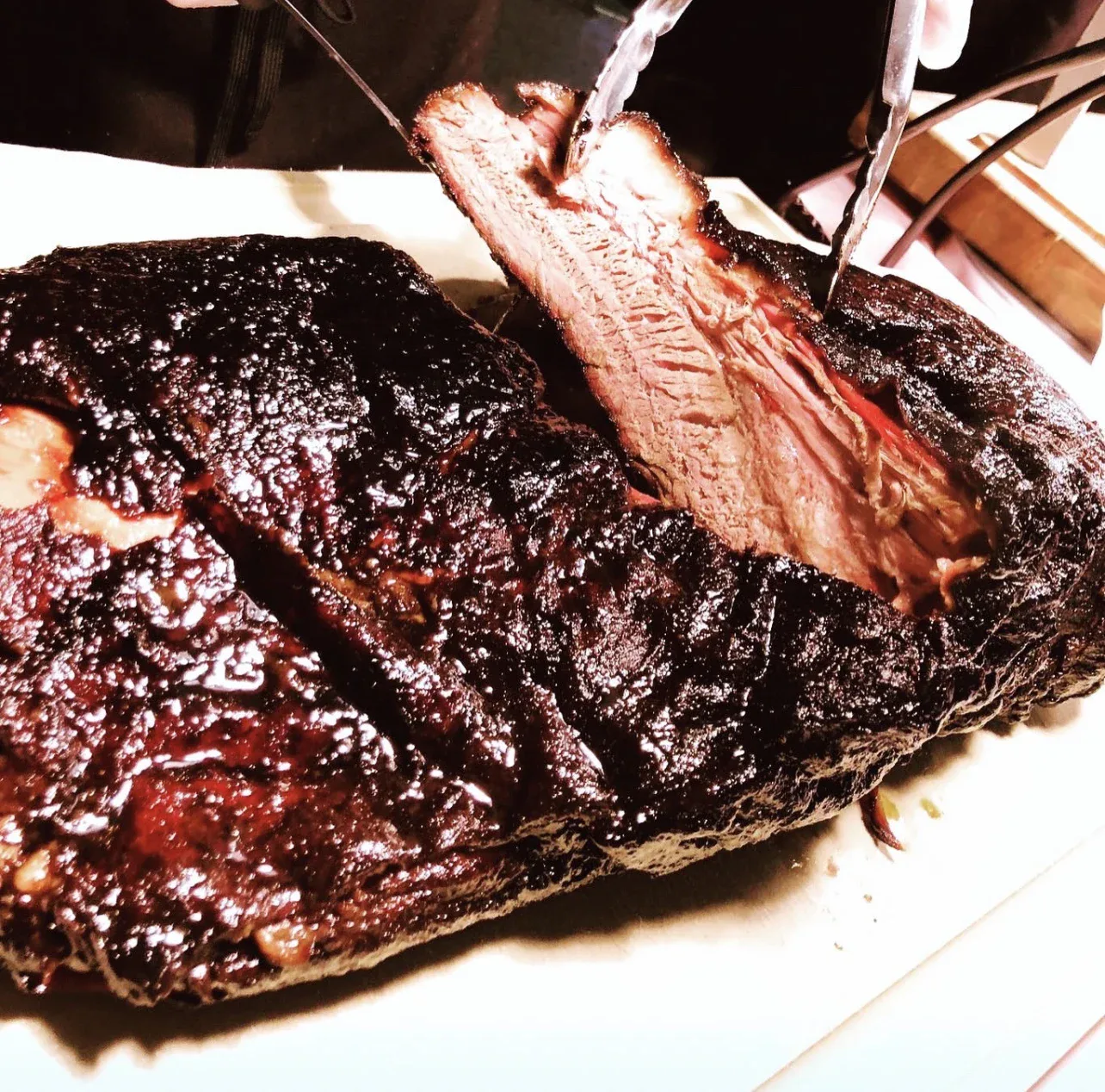 A thick slice of glazed smoked brisket lifted with tongs from the whole brisket