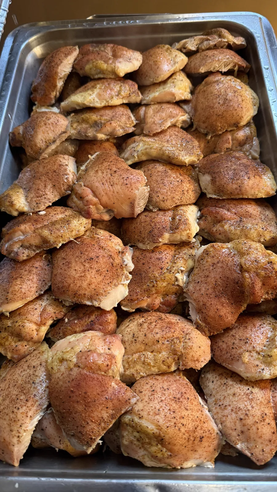 Seasoned chicken thighs packed into a steam table pan