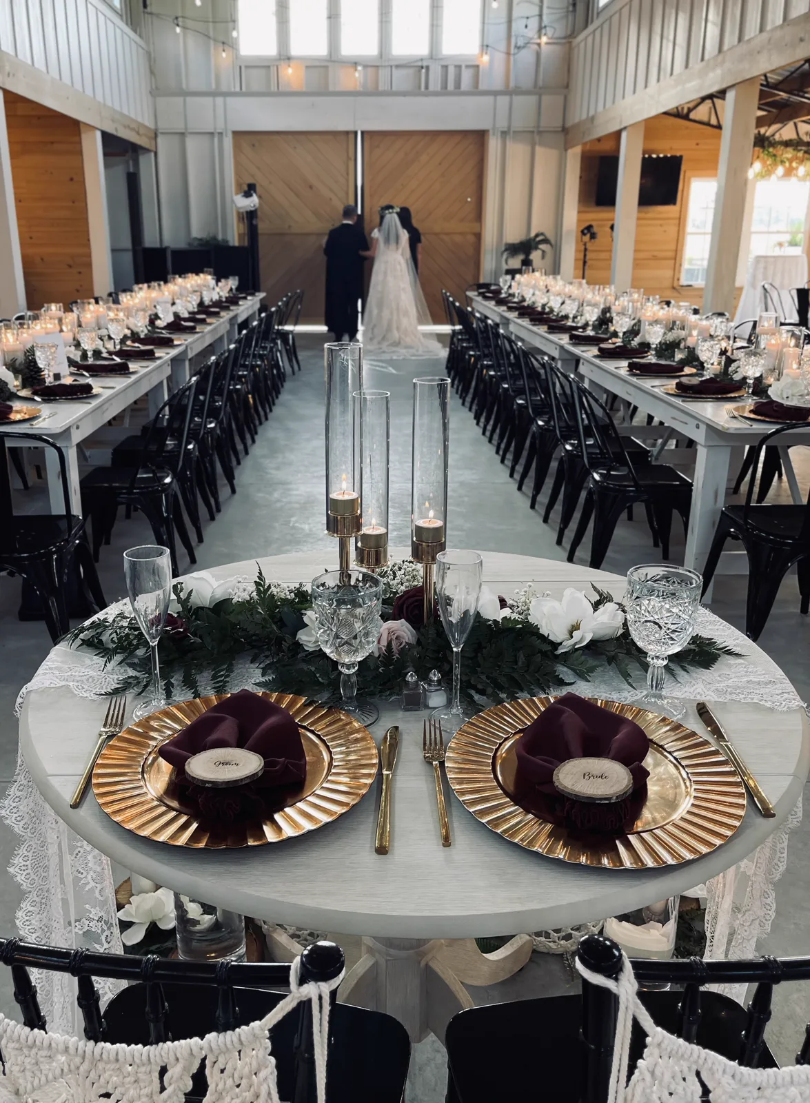 Round sweetheart table with gold chargers and Bride and Groom place cards, long tables with black chairs behind