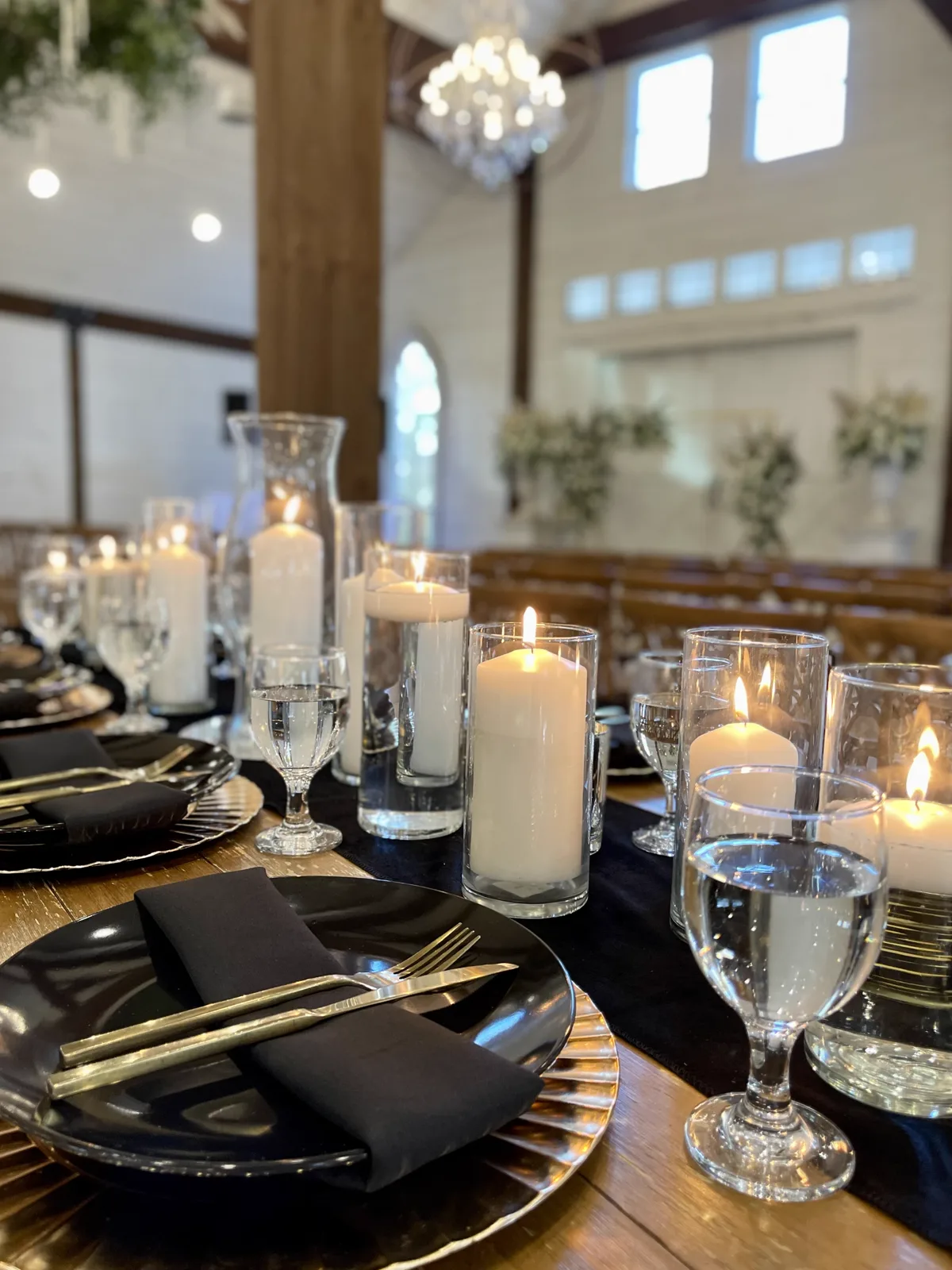 A long table set with black plates on gold chargers, black napkins, candles and glassware