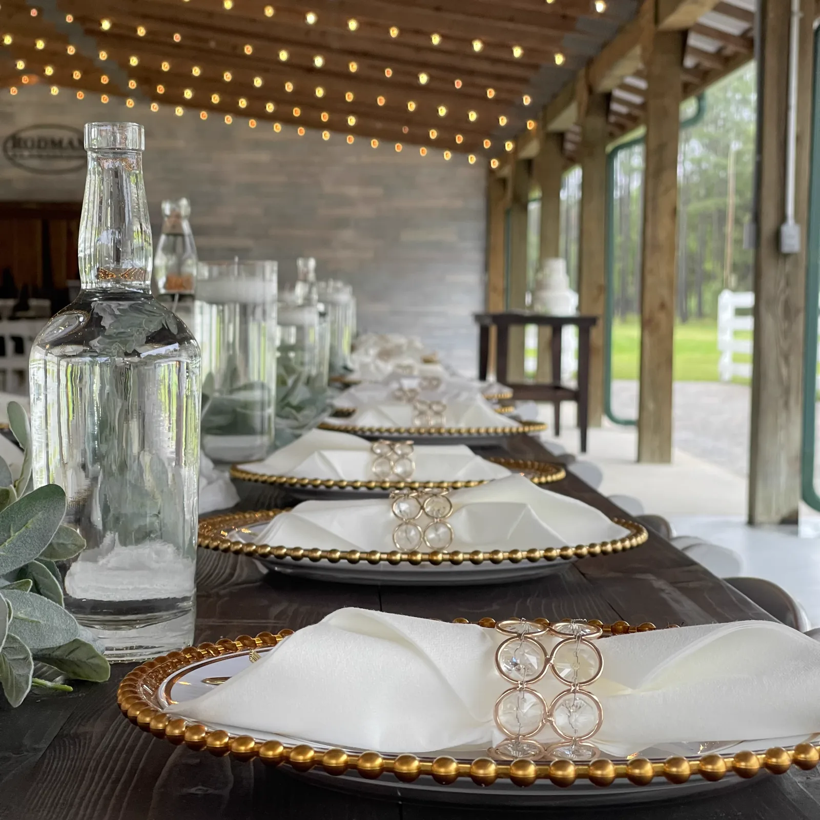 Gold beaded chargers with white napkins and crystal napkin rings beneath string lights
