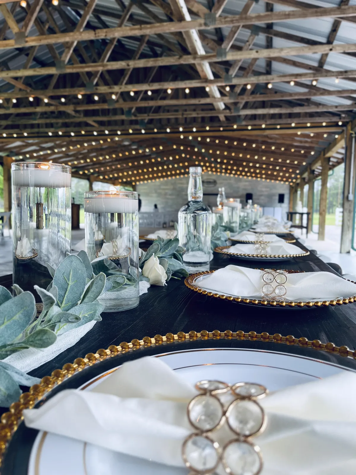 Gold beaded chargers and floating candles on a dark table under a pavilion strung with lights