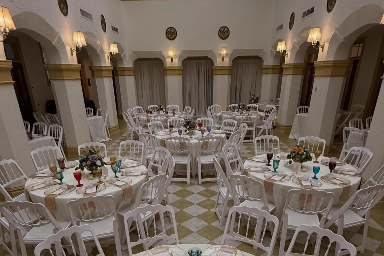 Round tables with gold rimmed chargers and colored glassware set under the arches of a historic hall.