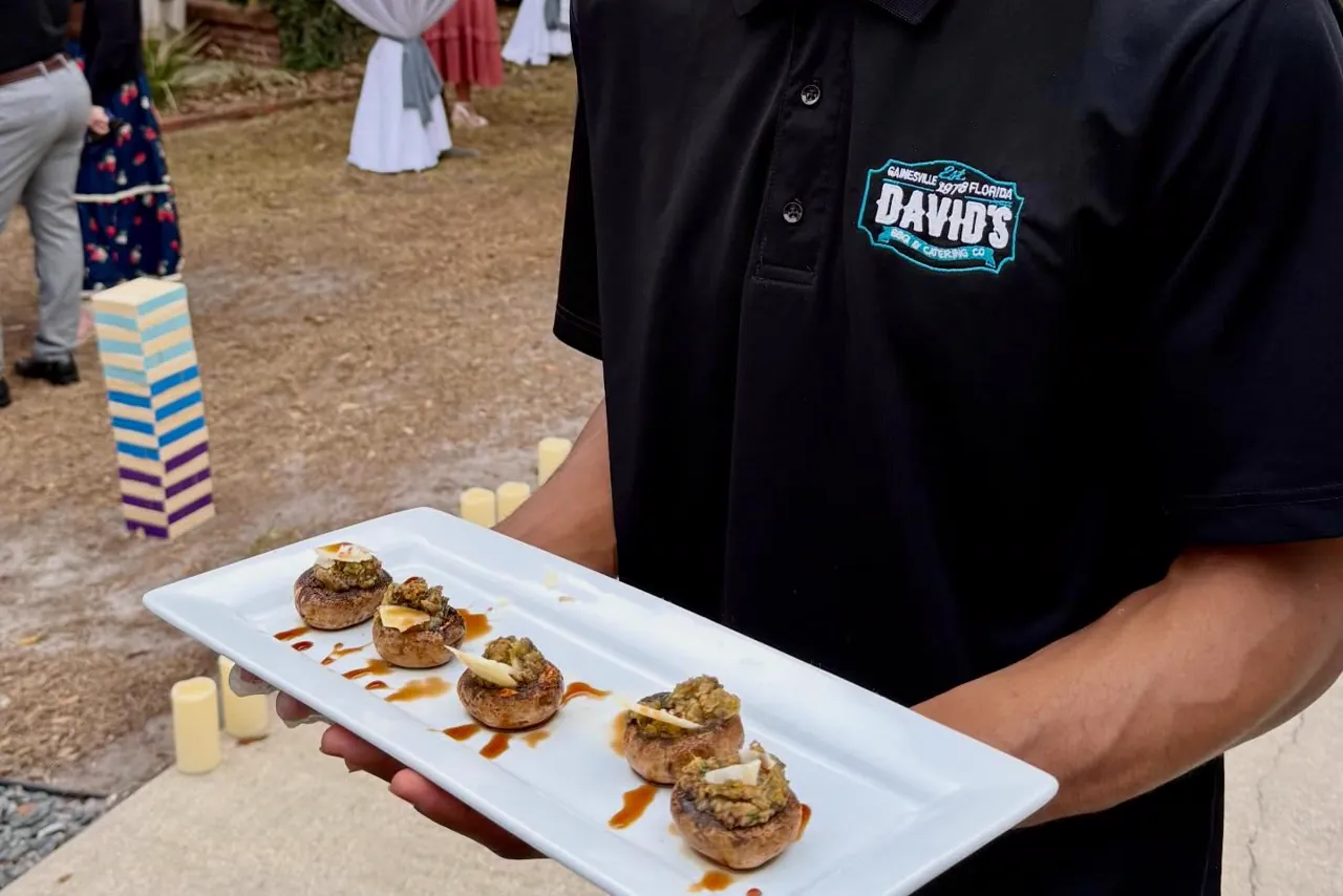 A David's server carrying a tray of stuffed mushrooms past guests at an outdoor reception.