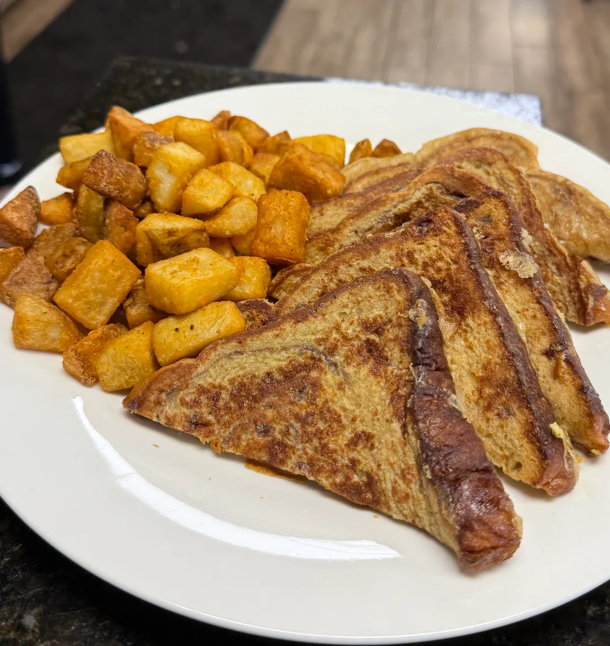 Three triangles of French toast beside home-fried potato cubes on a white plate